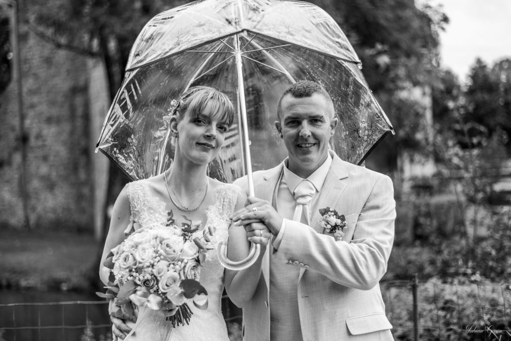Bérangère et Kévin posent enlacés dans un jardin, en tenue de mariage, devant un fond de verdure