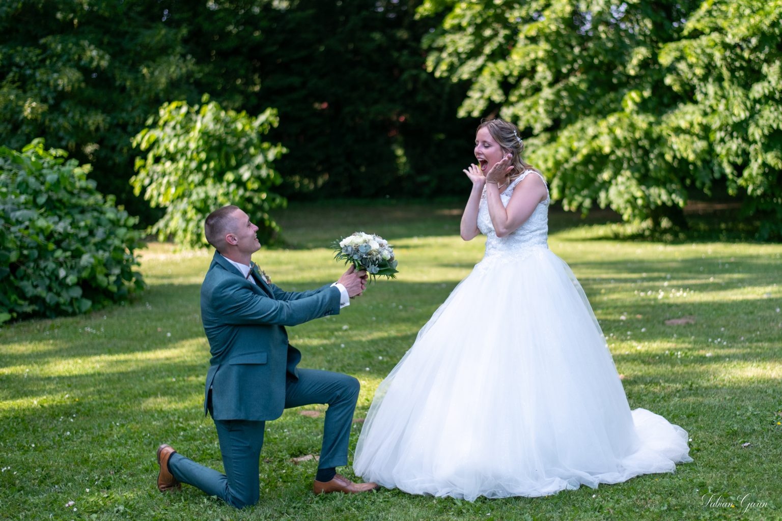 Photographe de mariage à Cambrai – Alexis à genoux offrant un bouquet à Emy au château de la Motte Fénelon.