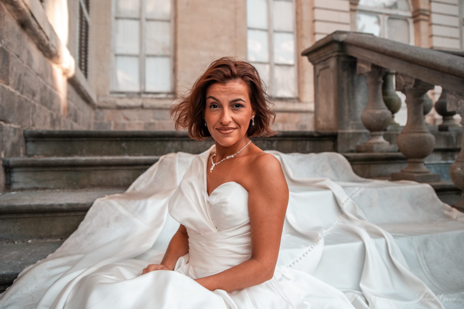 Portrait souriant de Maeva, en robe de mariée, assise dans une pièce élégante avant la cérémonie